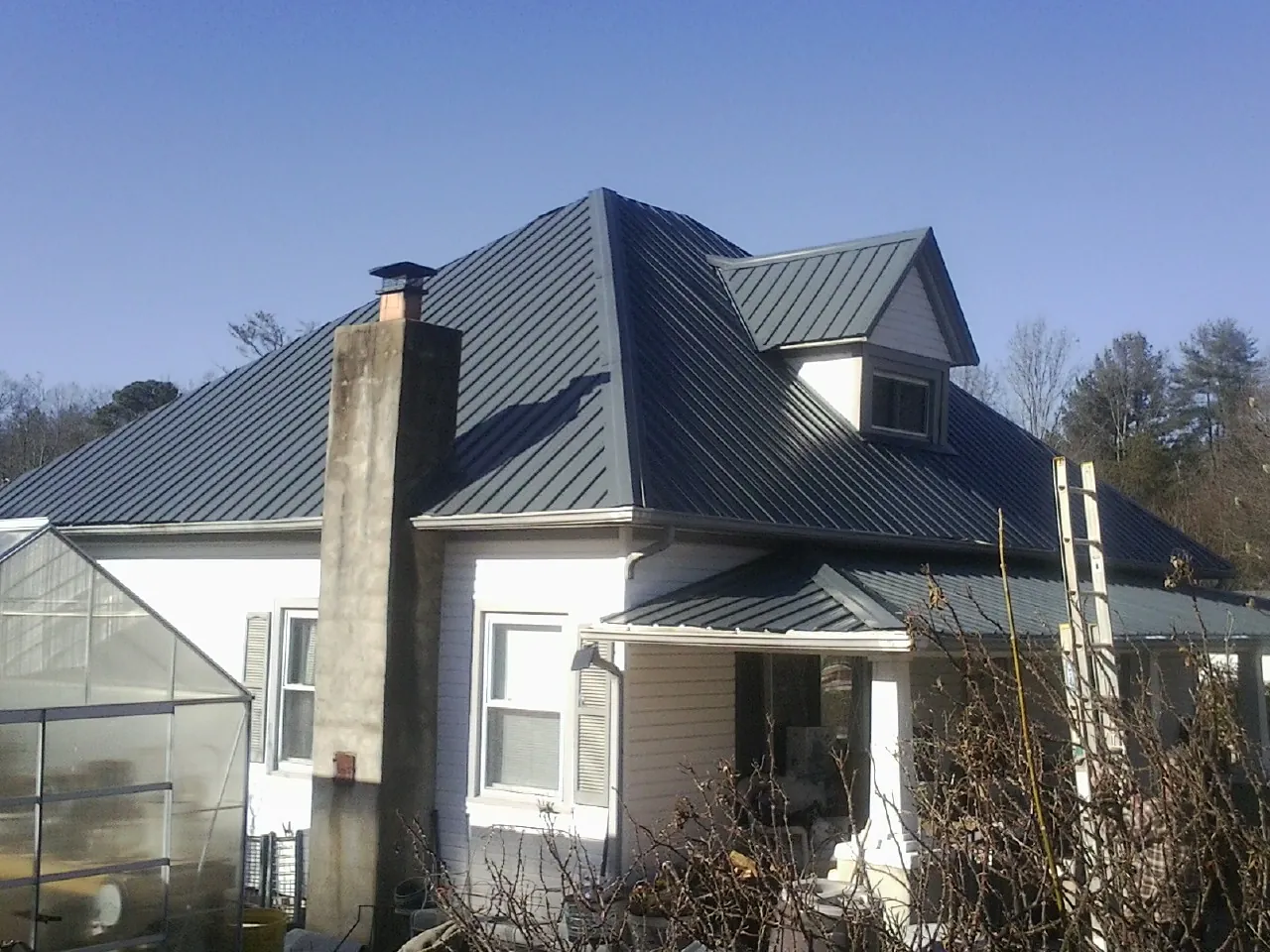Dark blue standing seam metal roof on a white farmhouse with dormer — Slate & Tile Roof Repair by Roofing Brothers in Steen