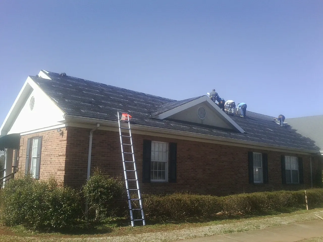 Crew tearing shingles off a brick ranch roof with a ladder set — Metal Roof Repair work by our crew in Steen
