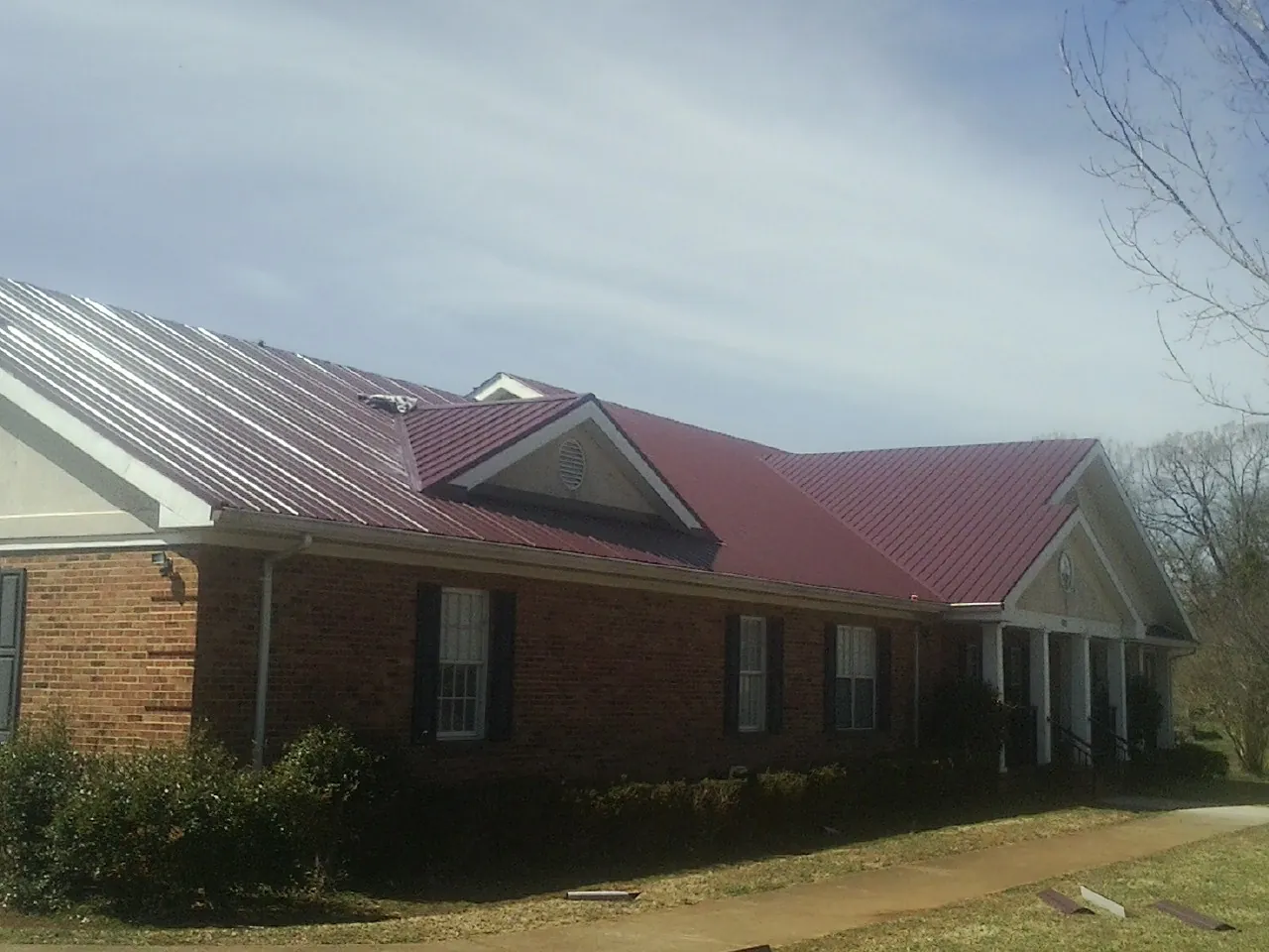 Red metal roof with gabled entries on a long brick building, from a Hail Damage Roof Repair job in Steen