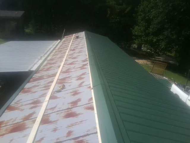 Old rusted panels beside newly installed green metal roofing — Wind Damage Roof Repair by Roofing Brothers in Steen