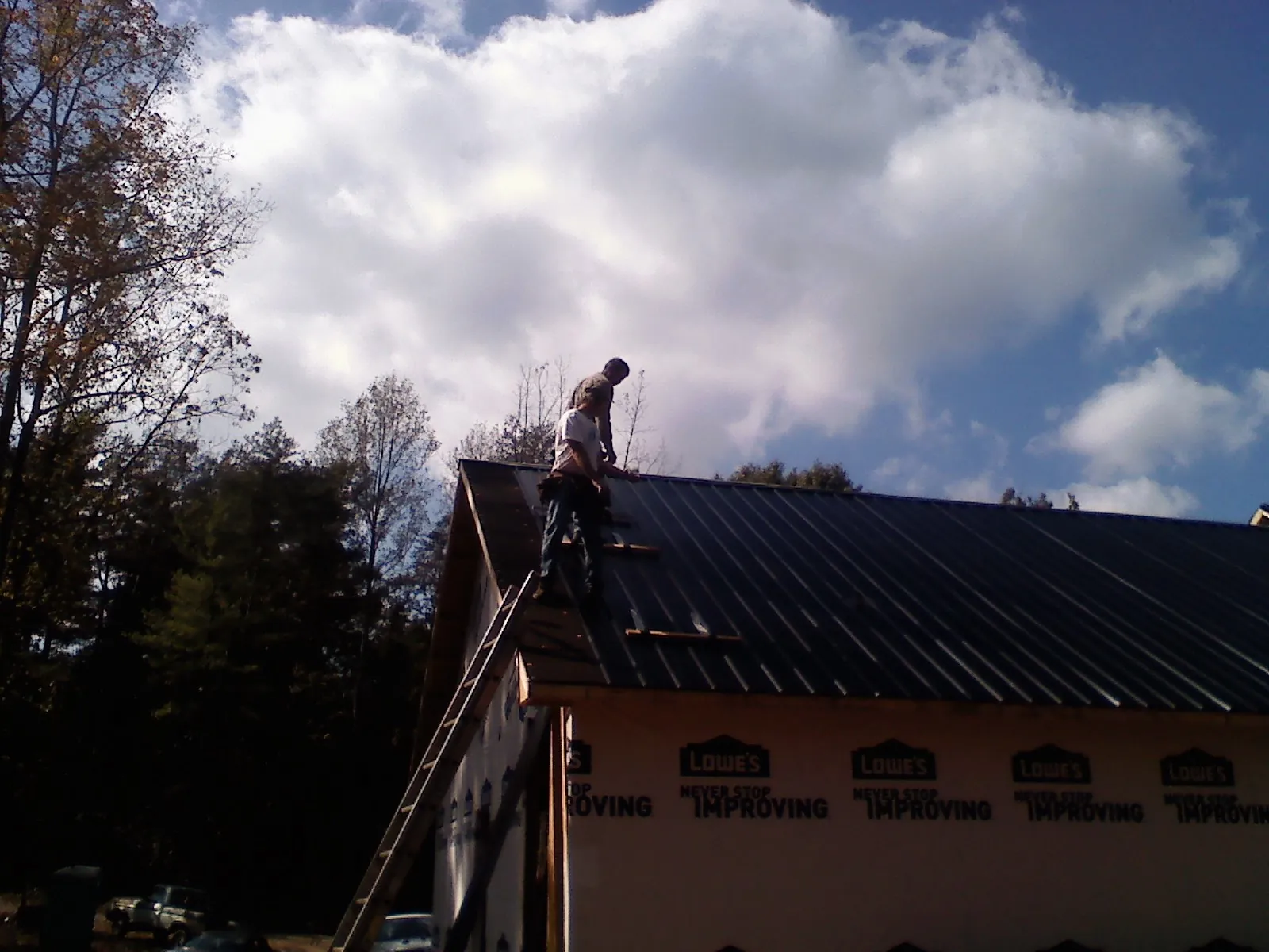 Roofer fastening dark metal panels high against a cloudy sky, from a Roof Inspection job in Steen