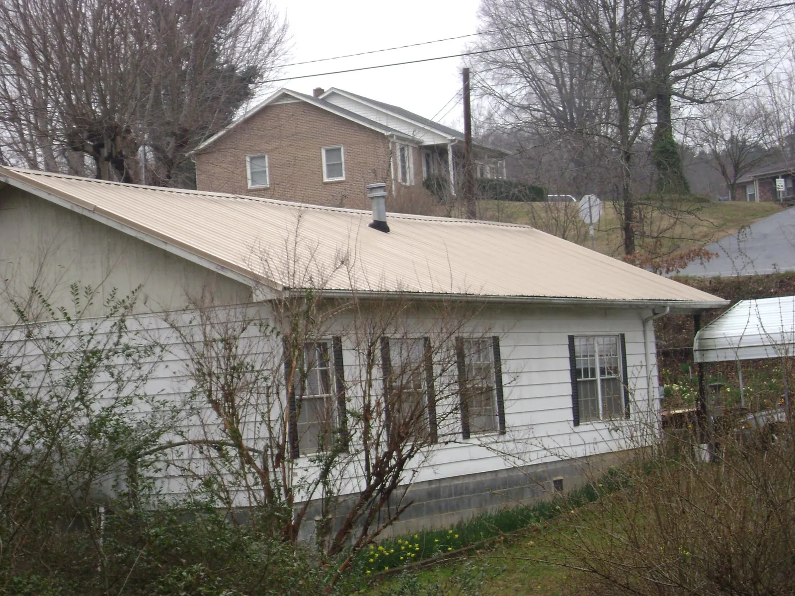 Tan metal roof on a white sided house set into a hillside — Commercial Roofing by Roofing Brothers in Steen
