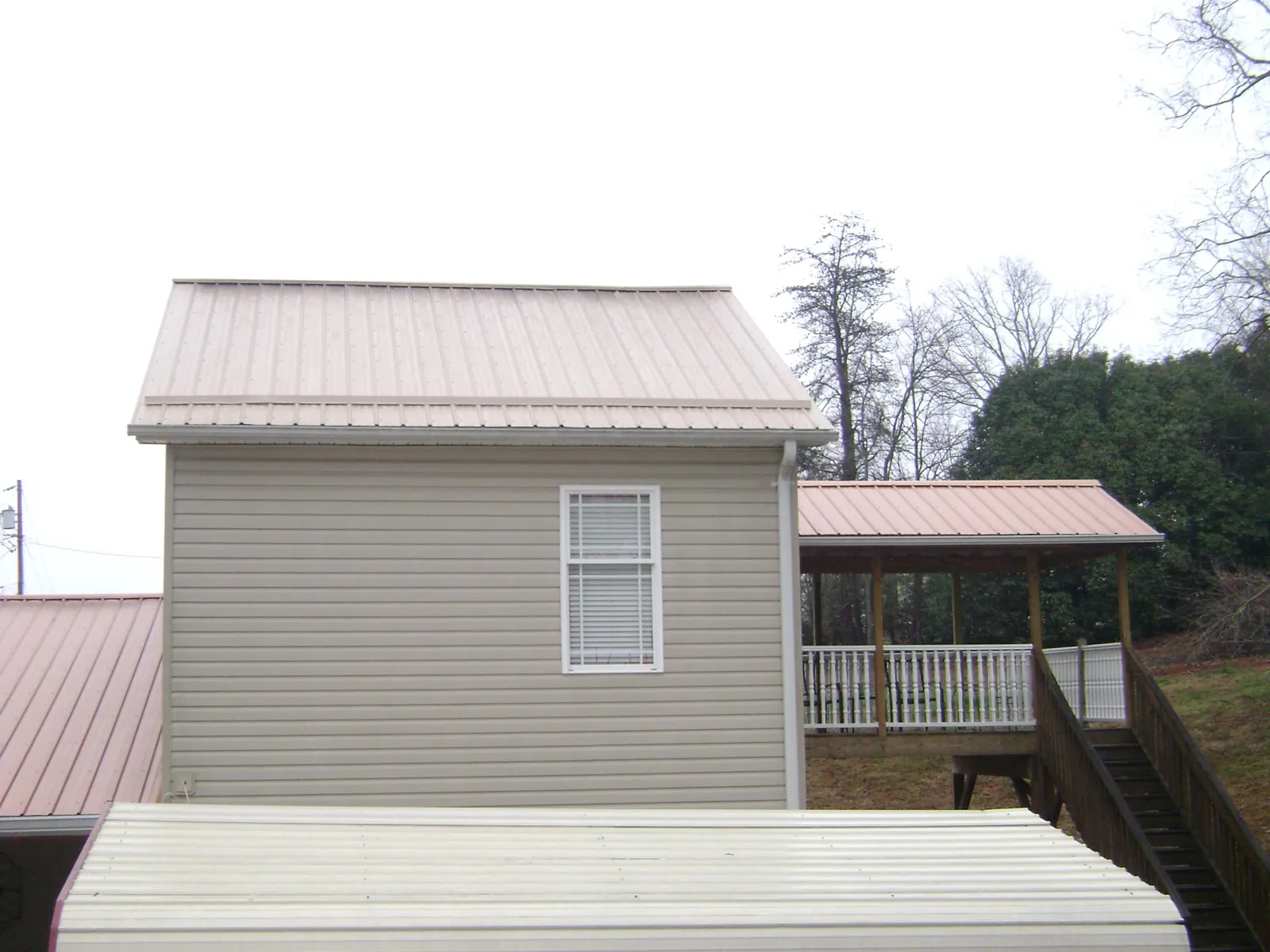 Tan metal roofs on a two story addition and attached porch, from a Roof Replacement job in Steen